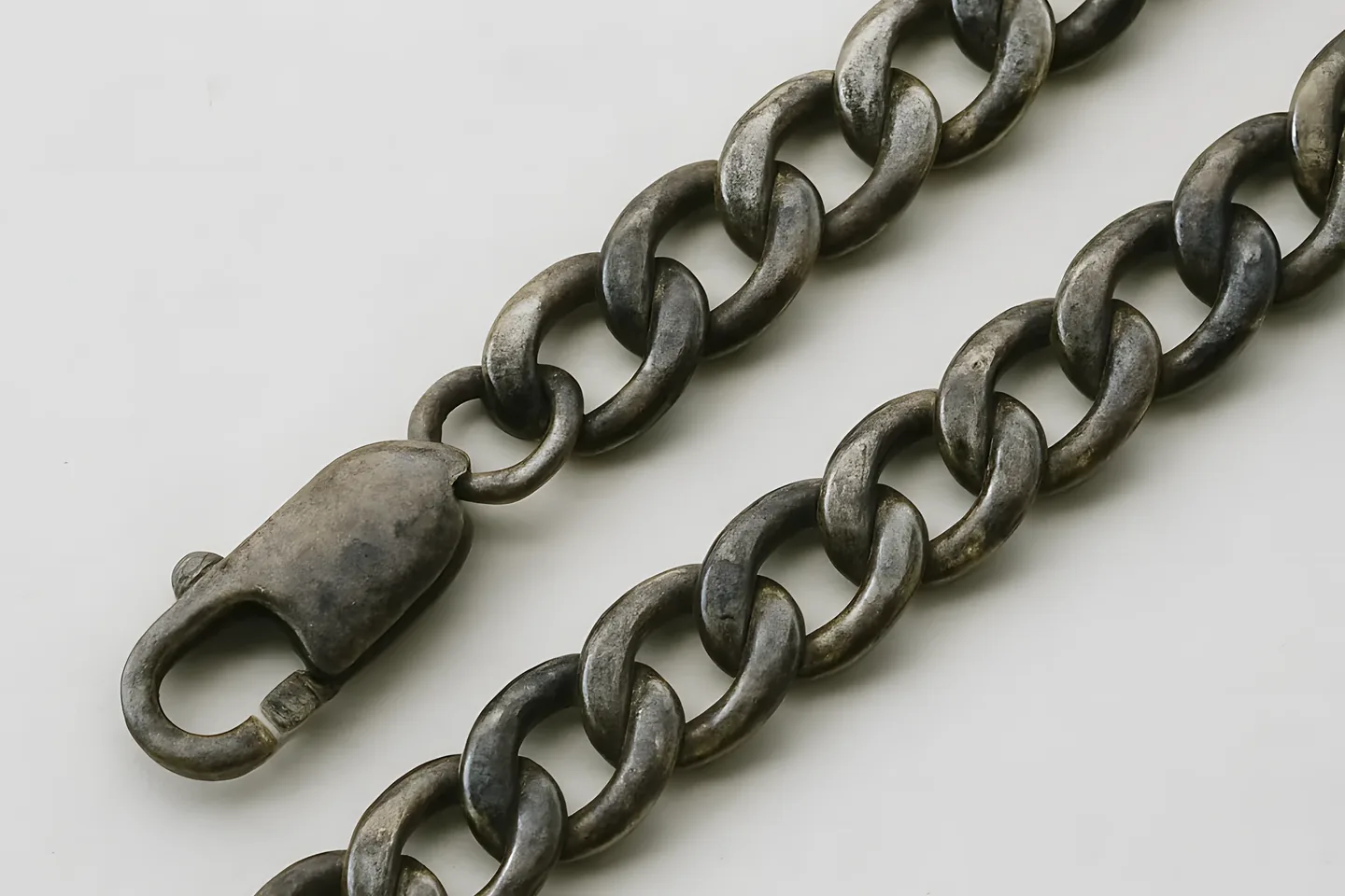 A heavy sterling silver curb chain darkened by tarnish, with the clasp in the foreground.