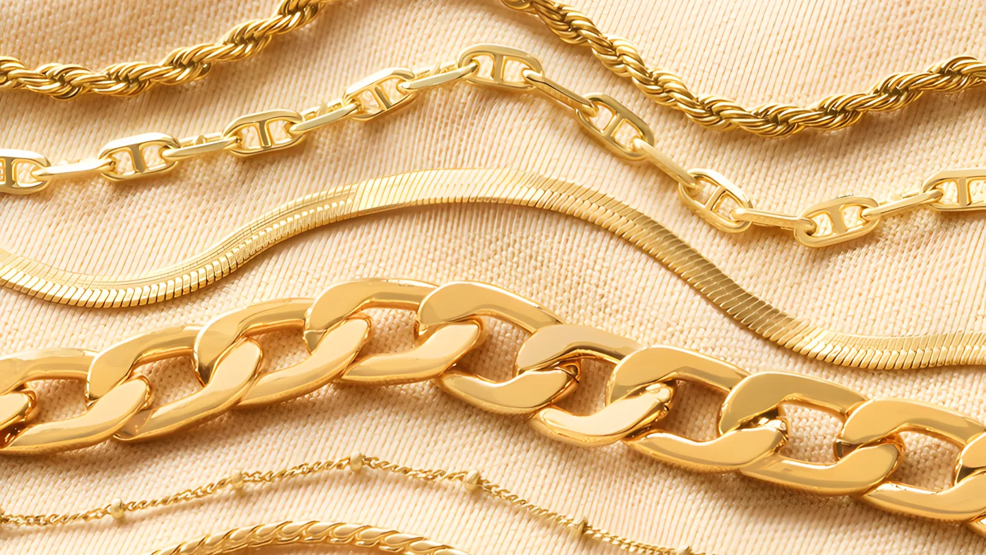 Five gold-coloured chains in different link styles laid side by side on cloth.