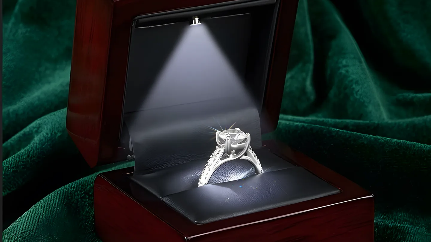 A diamond solitaire ring in a lit presentation box on green velvet.
